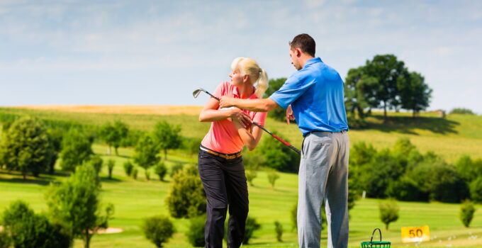 Young female golf player on course with an instructor. Depiction of golf teaching.